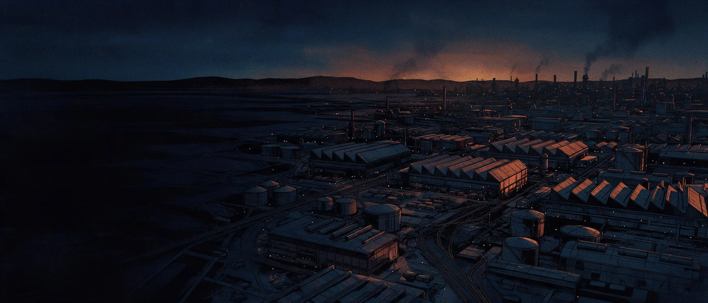 Aerial view of an industrial complex at dusk, with sawtooth-roofed halls, storage tanks and rail sidings